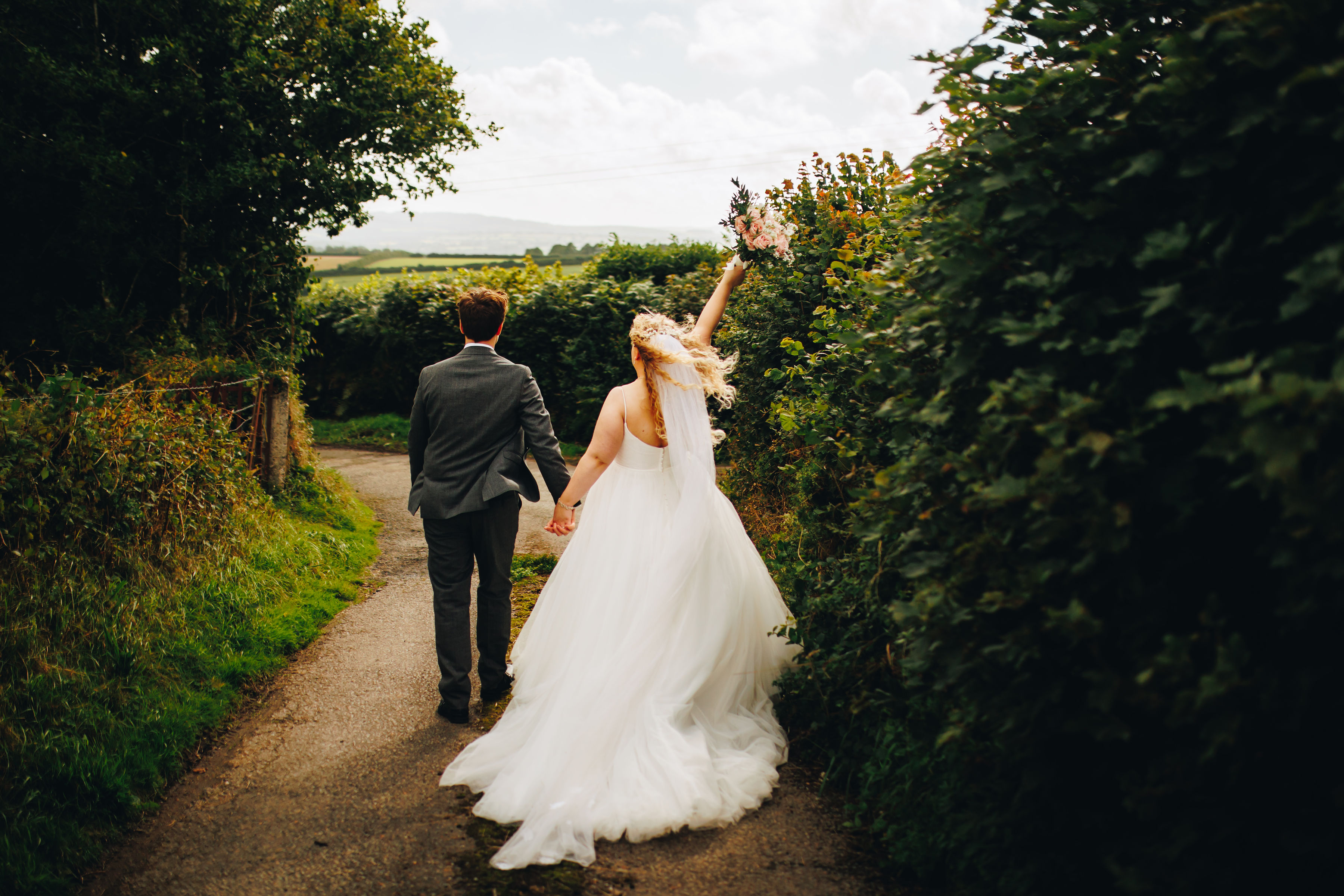 Couple photos at sunset, holding bouquet in the air with dress flowing in the breeze