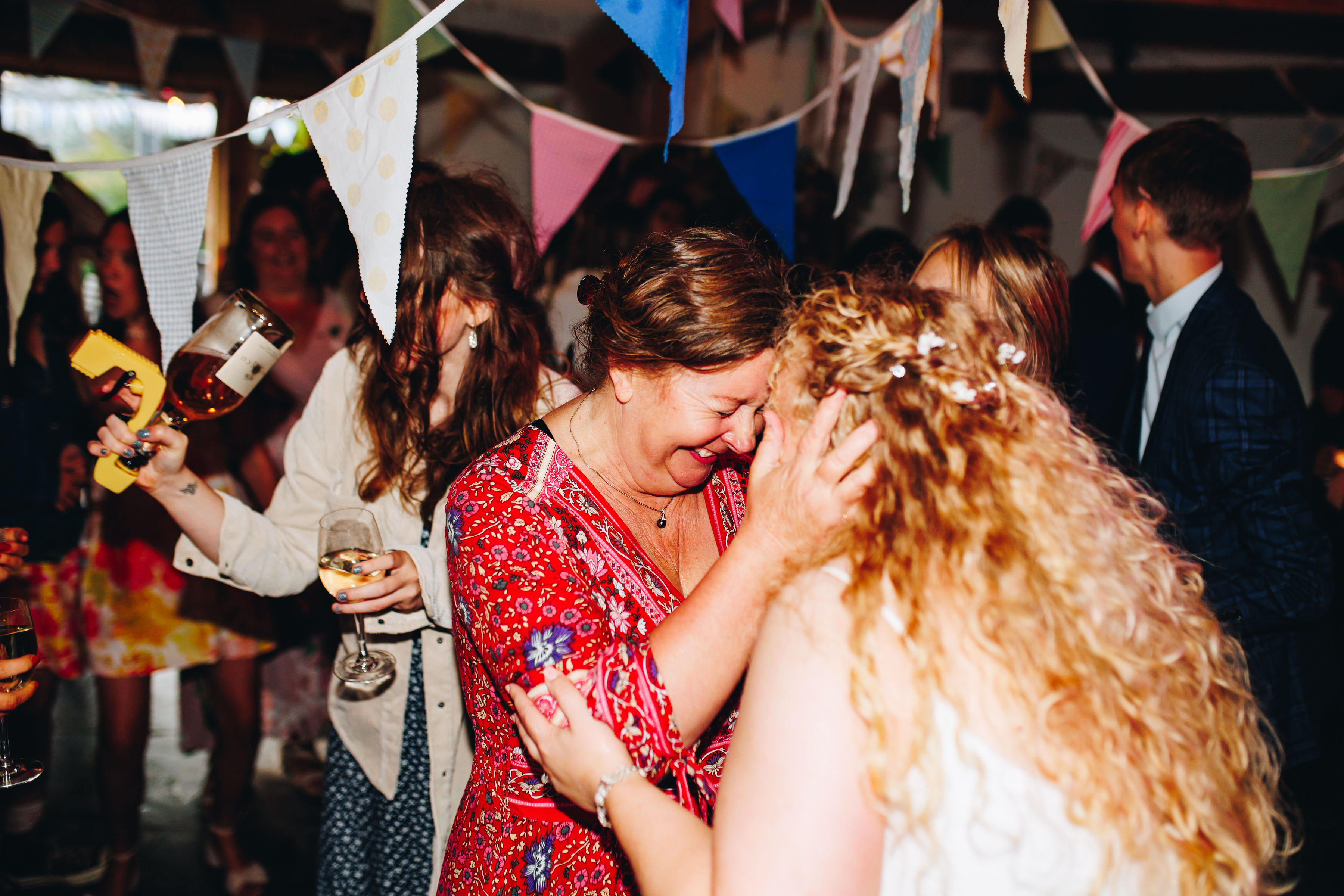 Bride and aunt holding each other forehead to forehead and smiling surrounded by dancing guests