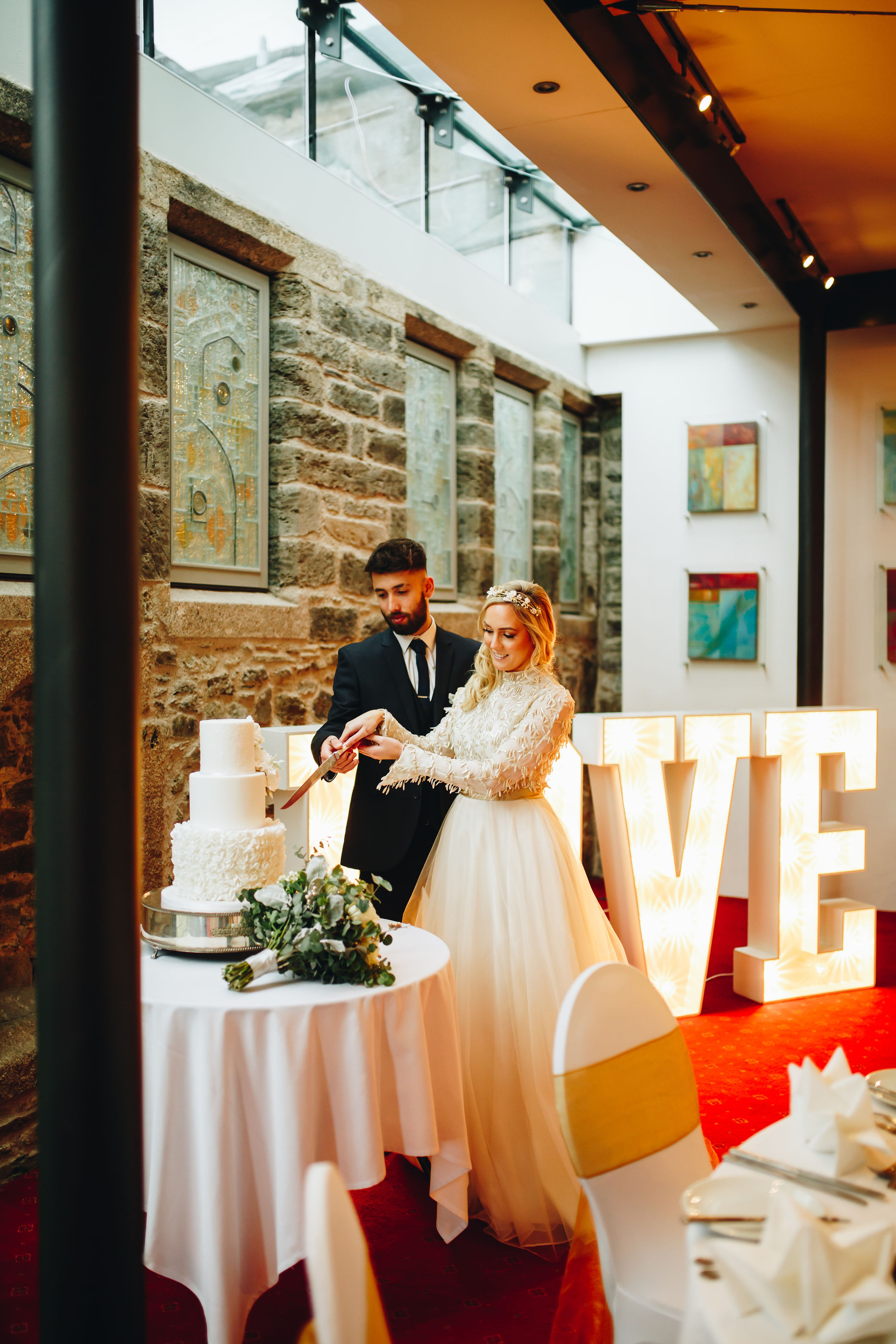 Bride and groom cutting wedding cake with giant 'LOVE' light up signs behind them