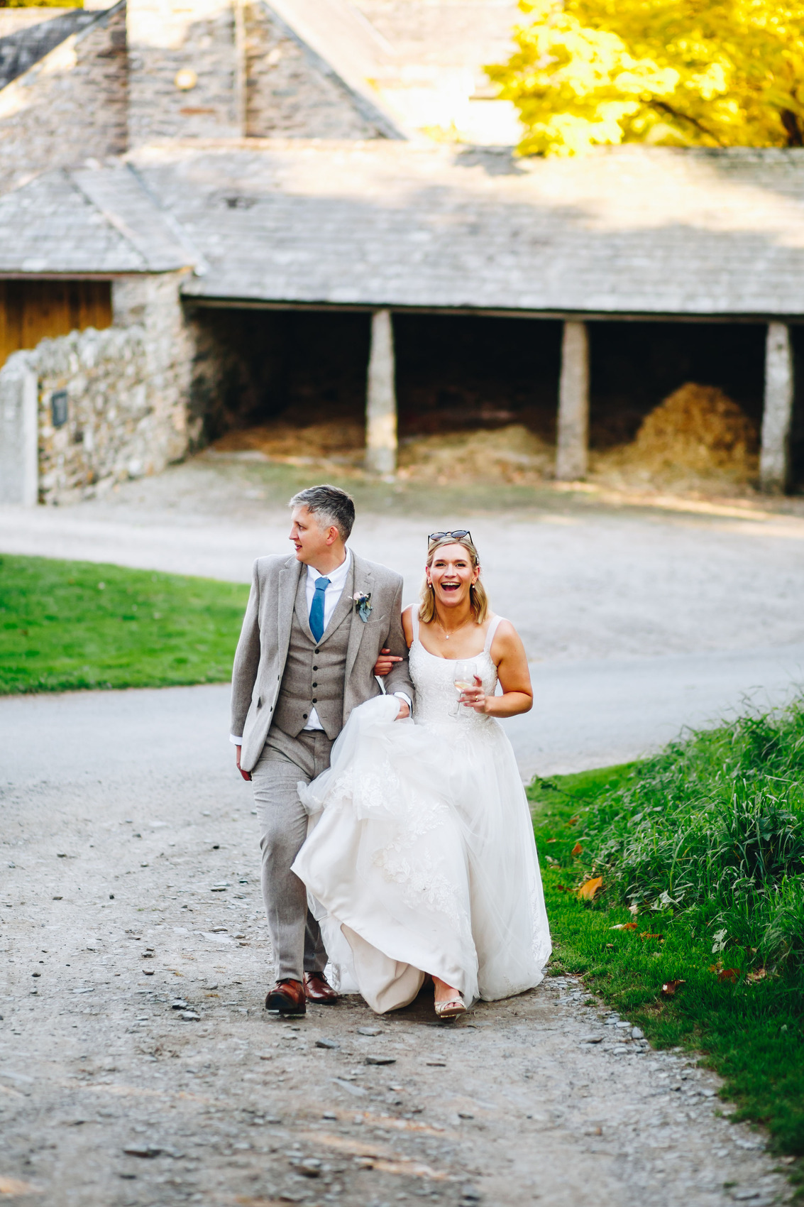 Bride smiling at the camera as she walks up a dirt path with her groom