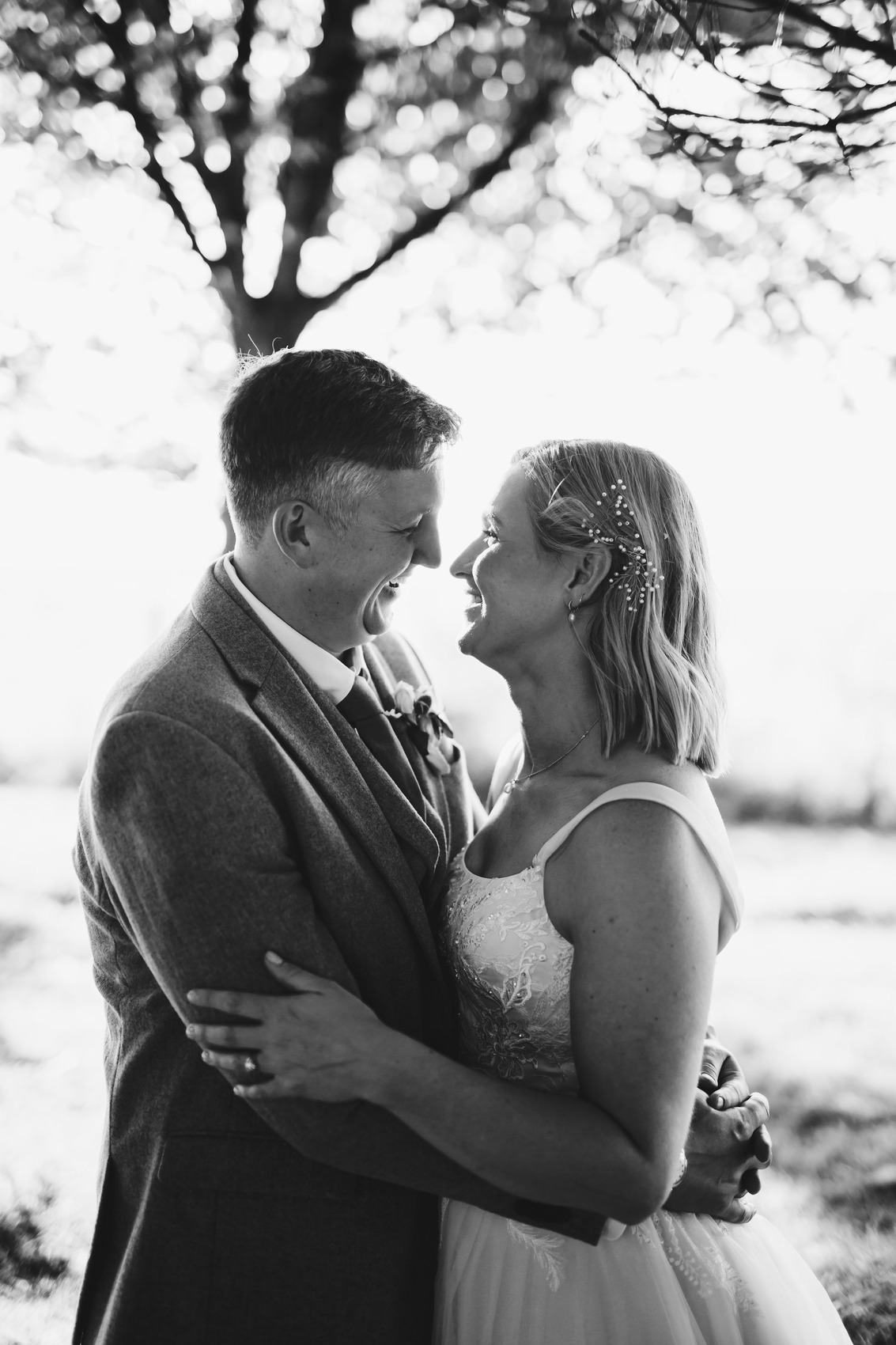 Black and white photo of bride and groom snuggling in a wooded area