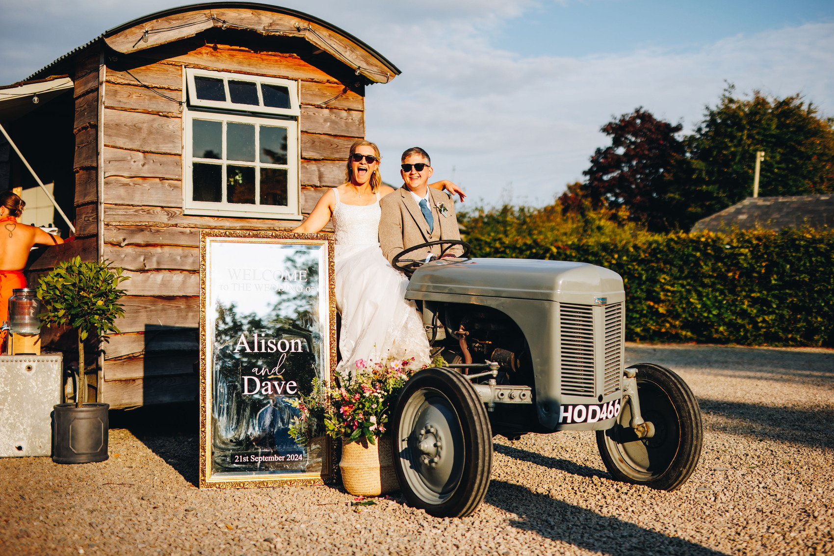 Bride and groom sat on an old tractor in the courtyard with sunglasses