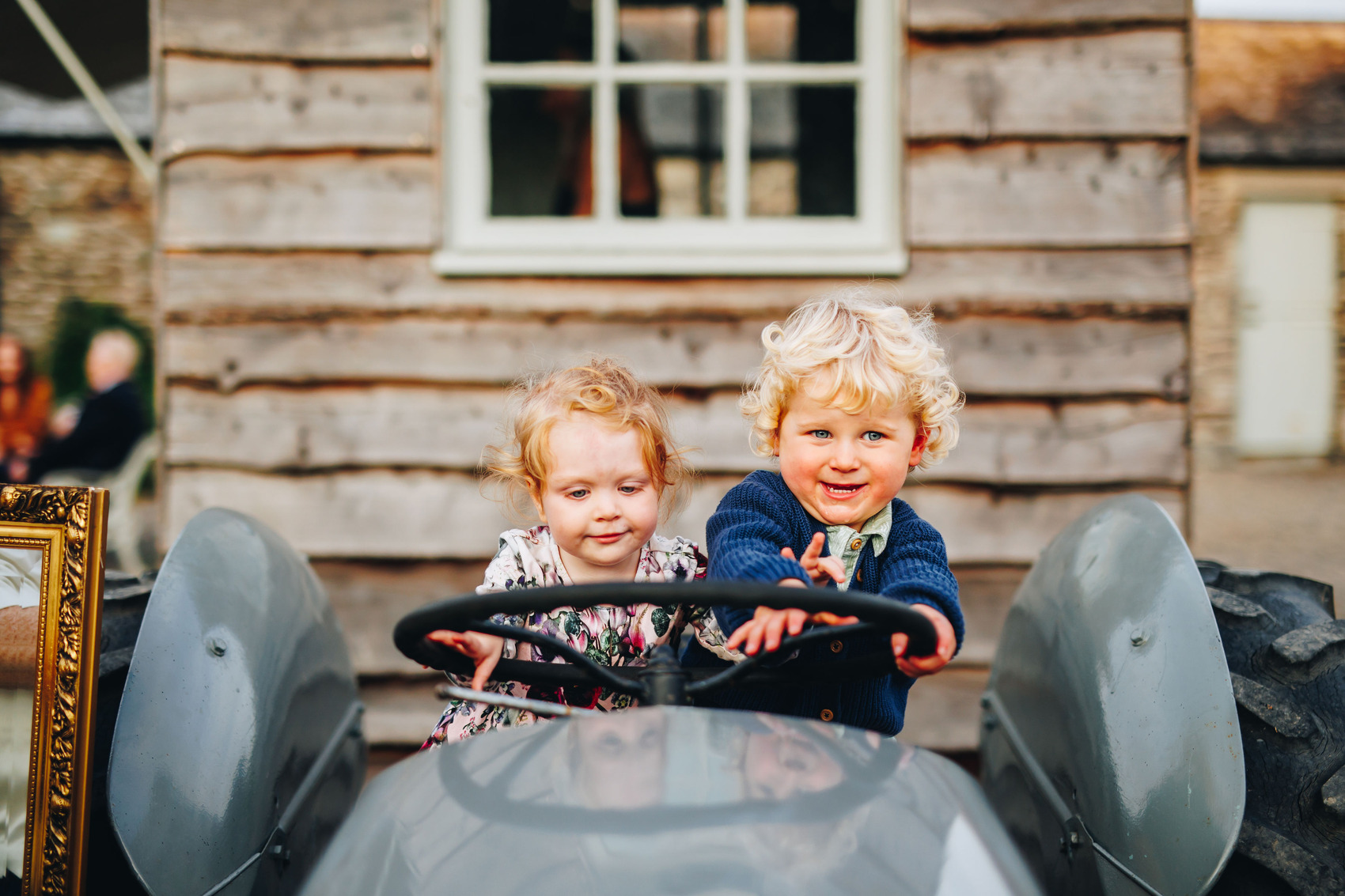 Two kids sat on an old tractor pretending to steer