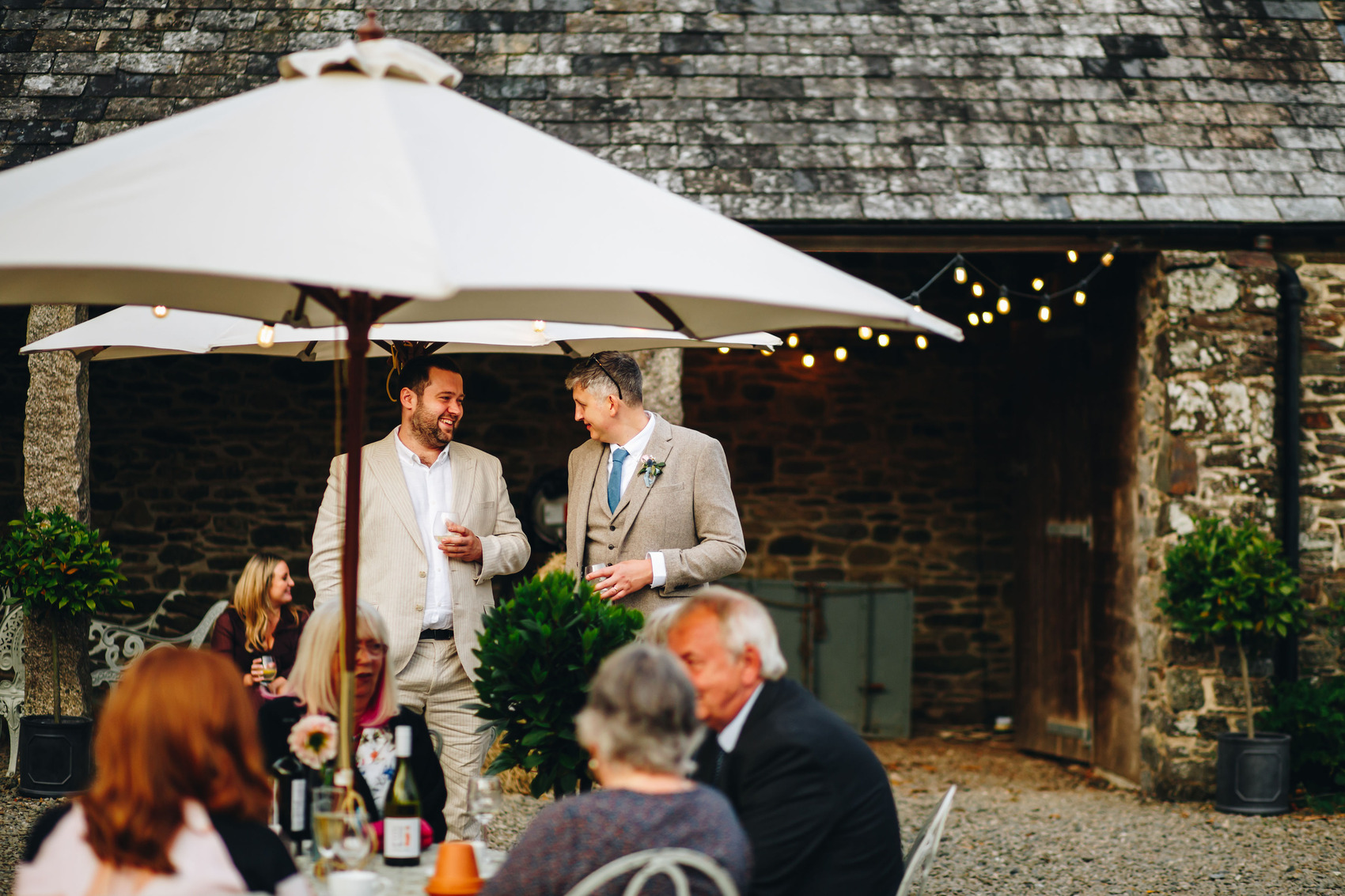 Groom and guest chatting outside under a parasol
