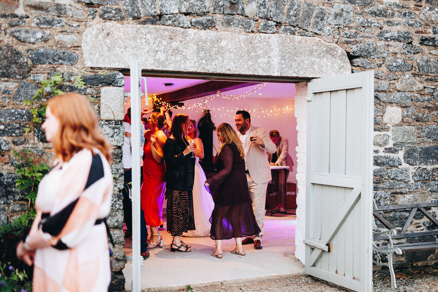 Photograph from outside, showing guests dancing inside through the barn doors