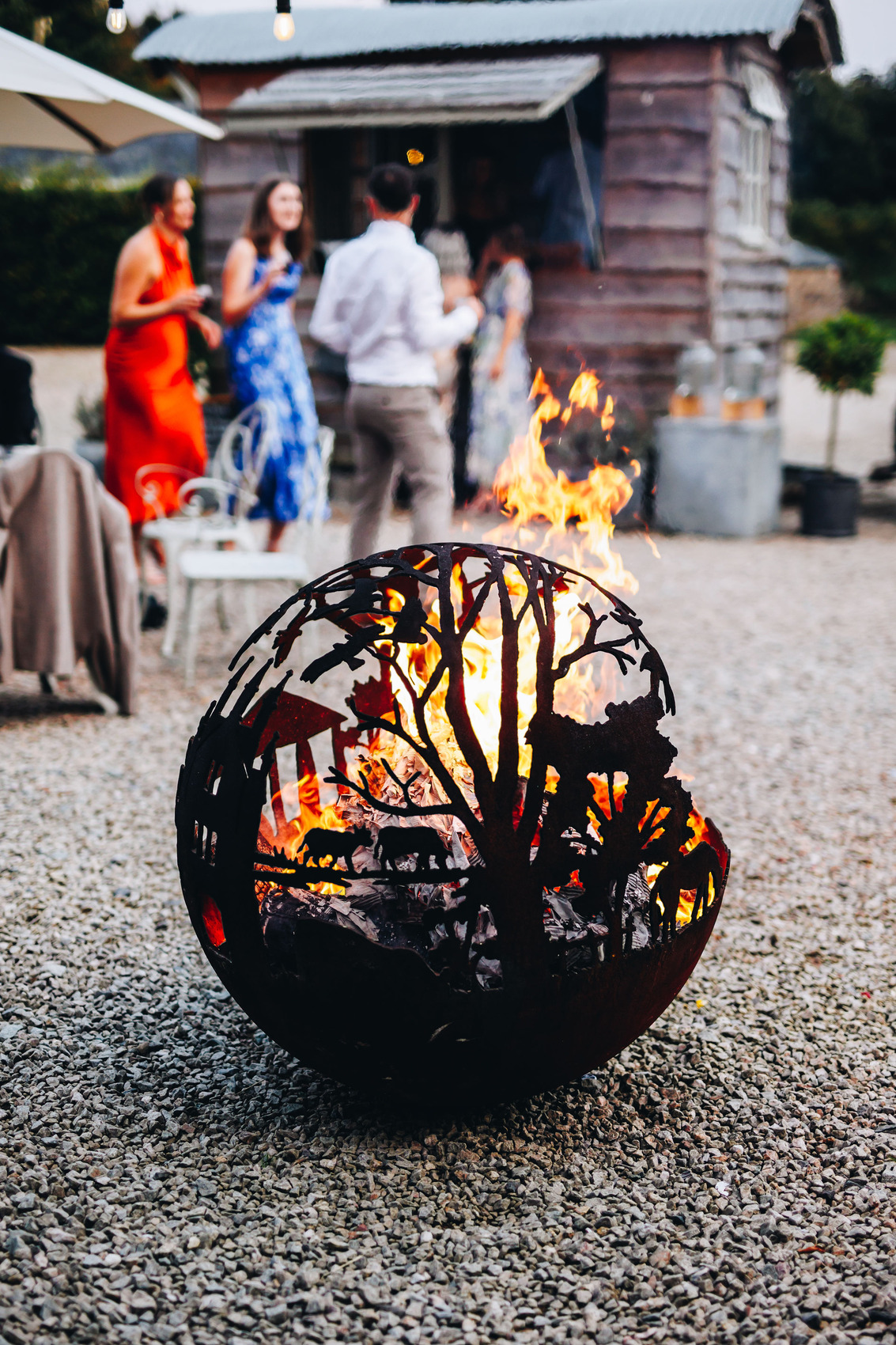 Circular fire pit with a woodland outline on it, in a gravel courtyard with wedding guests in the background
